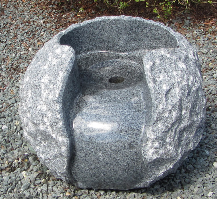 Diese Kugel mit ca. 30 cm Durchmesser aus massivem Granit wurde meisterhaft aus einem Stück gefertigt. Außen kunstvoll rau beschlagen und innen poliert, zeigt sie den schönen Kontrast des Natursteins. In der Mitte ist eine Bohrung von ca. 25 mm mit kleine